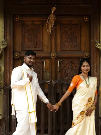 A couple in traditional South Indian attire poses in front of an ornate temple door for their pre-wedding shoot.