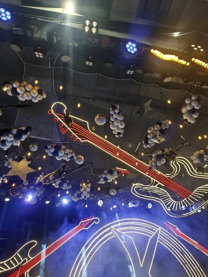 A stunning view of a rock-and-roll themed ceiling. The space is filled with neon guitars, balloon clouds, and spotlights, creating an electrifying atmosphere perfect for a music festival-style party.