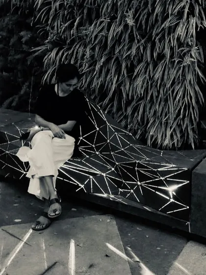A black and white photo of the architect sitting on the illuminated "Origami" bench. The image captures a quiet moment, showcasing the bench as both a functional object and a piece of light art.