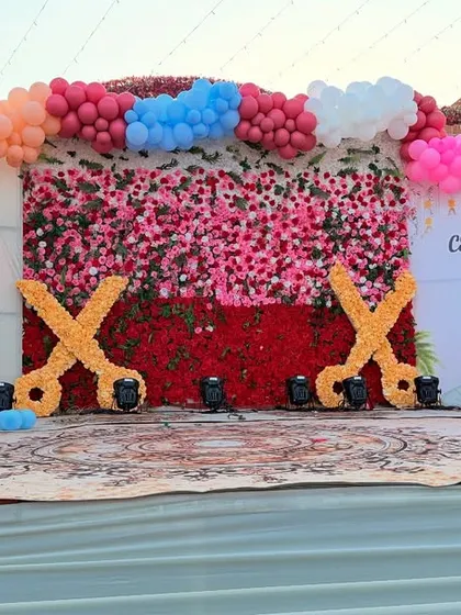 A daytime view of the Mundan ceremony stage, showing the bright colors of the balloon arch and the floral wall.