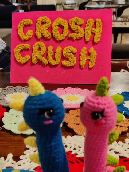 Two cute dinosaur figures in front of my crochet business sign at a stall.