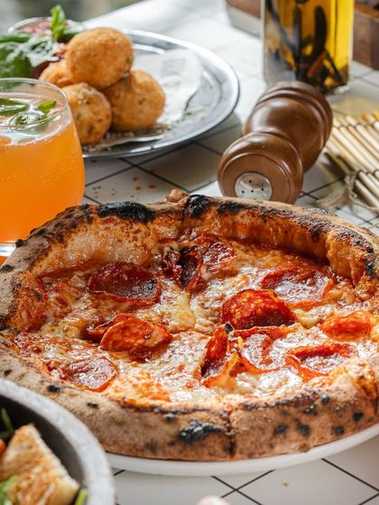 A perfect Sunday spread. Our pepperoni pizza is the star, surrounded by fresh sides and drinks, making for an ideal meal with friends.