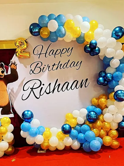 A cute Masha and the Bear theme for a second birthday. This simple yet charming setup includes a character cutout and a balloon arch in blue, yellow, and white around a personalized backdrop.