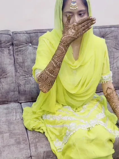 A bride in her beautiful yellow outfit, giving a glimpse of her elaborate elbow-length mehndi design.