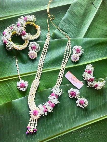 A complete floral jewellery set made with fragrant jasmine buds and pink flowers. This set includes a necklace, maang tikka, earrings, and bracelets.