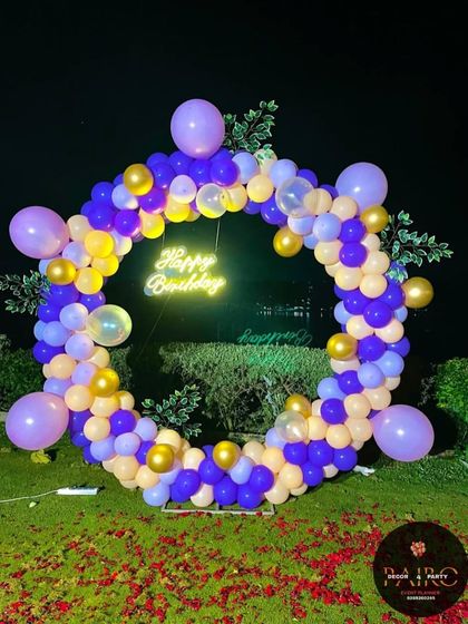 An elegant purple and gold balloon ring set up in a garden for a milestone birthday celebration.