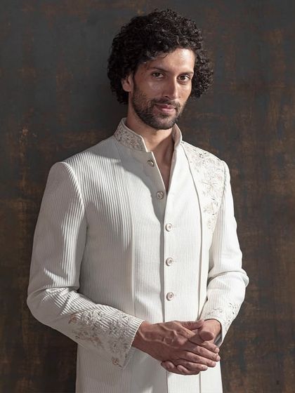 A closer look at the fine details of the asymmetrical ivory sherwani. Notice the textured fabric and the precise placement of handwork, designed to draw the eye without overwhelming. This is the essence of quiet power.