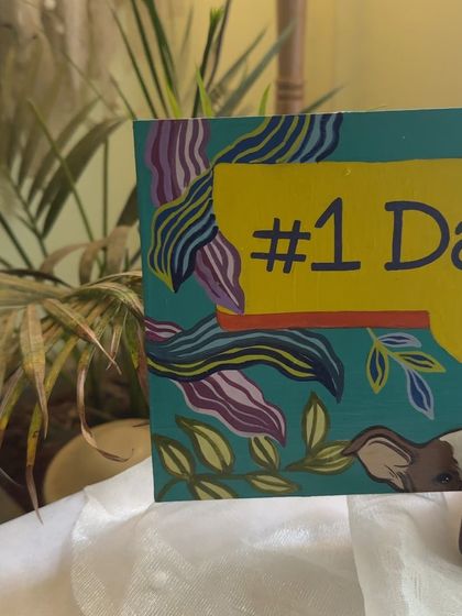 A "#1 Dad" desk plaque painted for a new father, featuring him with his baby and fur baby peeking into the frame.