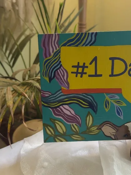 A "#1 Dad" desk plaque painted for a new father, featuring him with his baby and fur baby peeking into the frame.