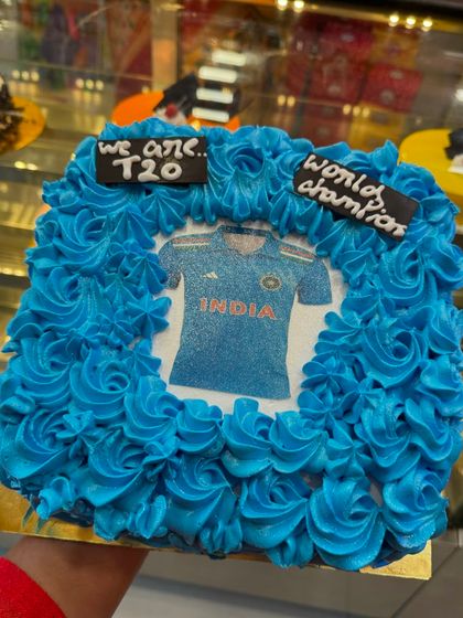 A celebratory cake for India's T20 World Cup win. This photo cake features the Indian team jersey, framed with blue frosting rosettes, perfect for celebrating a national victory.
