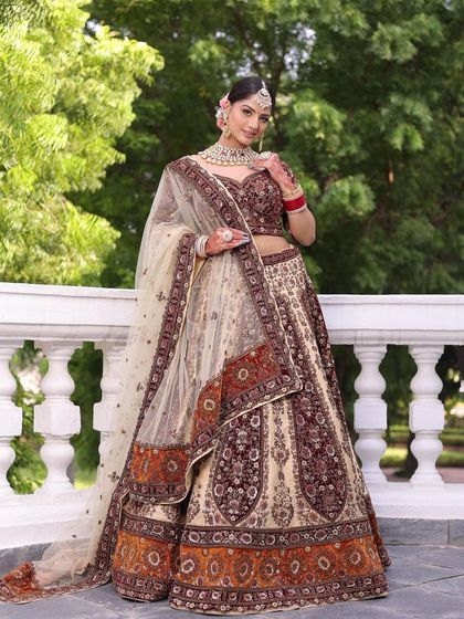 A full-length shot of a bride in a unique beige and maroon lehenga. This is a great option for brides who want a traditional feel with a non-traditional color palette.
