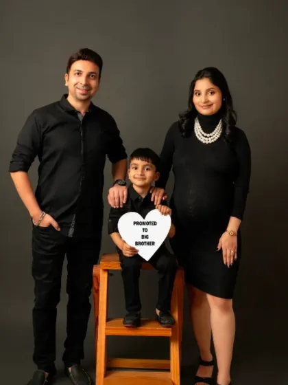 Celebrate your growing family with a portrait that includes everyone. This classic black turtleneck dress is perfect for coordinated family photoshoots, and the "Promoted to Big Brother" sign adds a touch of sweetness.
