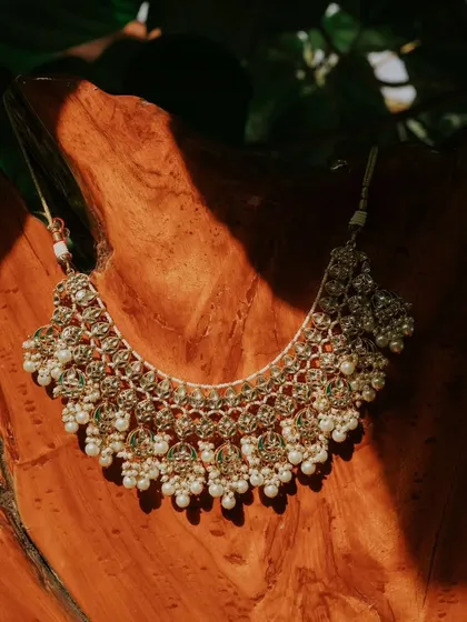 The bride's necklace is artfully displayed on a piece of wood, with natural light highlighting its intricate design. We love finding creative ways to photograph your special details.