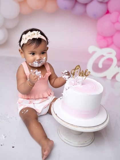 She's getting into the spirit of the cake smash, with frosting on her hands and a happy look on her face.