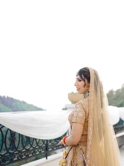 A serene portrait of the bride looking out from a balcony. The mountain landscape in the background adds a sense of peace and grandeur to her wedding day look.
