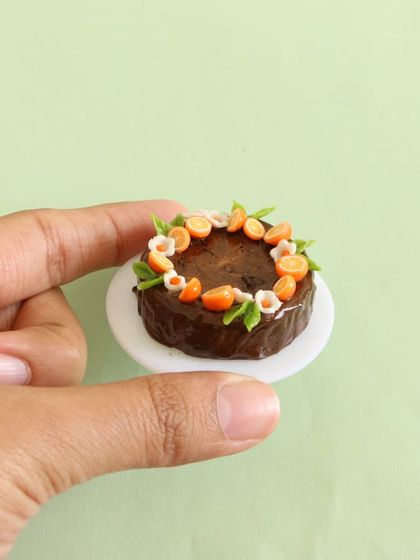 A close-up of a miniature chocolate fruit cake, with tiny orange slices and flowers.