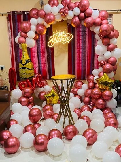 A beautiful home setup with a balloon arch in rose gold and white, a champagne bottle balloon, and 'LOVE' foil letters.