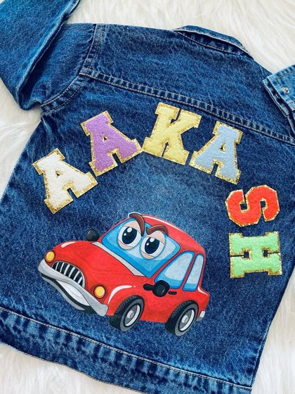 A personalized denim jacket with a car theme for 'Aakash'. His name is spelled out in colorful letters around a large, cartoonish red car patch, perfect for any little vehicle enthusiast.