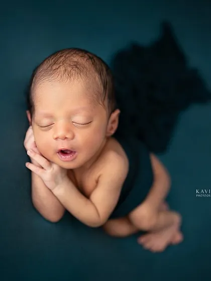A newborn rests in a classic pose against a deep teal backdrop. The simplicity of the setup allows the baby's perfect form and peaceful expression to be the hero.