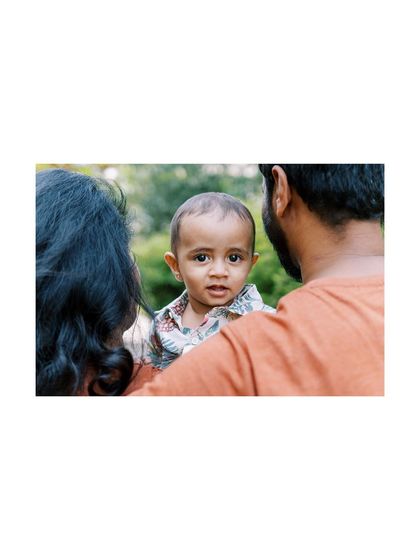 A candid shot of a baby looking over his parents' shoulders after a fun cake smash session.
