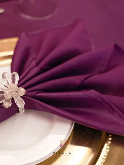 The beauty is in the details. A simple purple napkin is transformed with an elegant fold and a sparkling crystal napkin ring, sitting atop a gold charger plate.