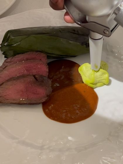 Plating a tenderloin dish with mole and avocado crema. The squeeze bottle allows for precise placement of sauces.