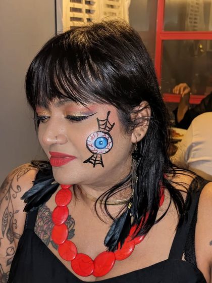 A spooky and artistic Halloween look, featuring a realistic eyeball caught in a spiderweb on the cheek.