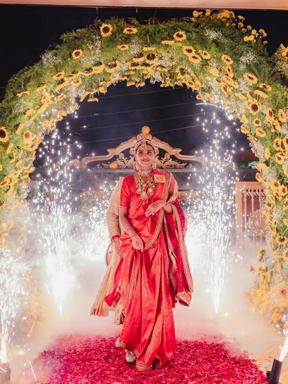 Manisha's grand entrance in her red Sabya saree. The sparklers and flower petals create a dramatic and celebratory welcome for the bride.