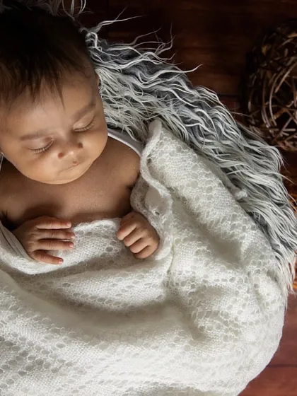 Here, I used a soft white blanket to gently wrap the baby, creating a sense of security. The dark, textured background provides a beautiful contrast, making the peaceful newborn the central focus.