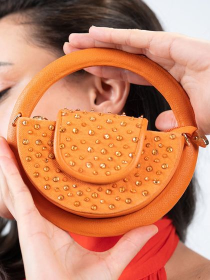 A bag that looks good enough to eat. This is a close-up of my orange semi-circle mini bag, showing the crystal stud details and the unique circular handle that makes it a standout piece.
