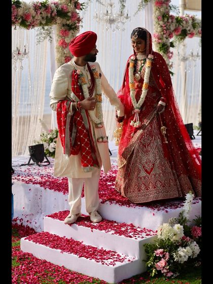 A wide shot of a Sikh wedding ceremony, with the couple on stage surrounded by rose petals. This image captures the scale and beauty of the wedding rituals.