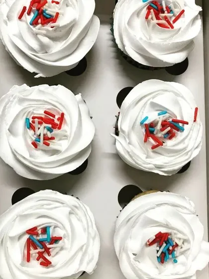 Simple, classic, and delicious. This top-down view shows six of our homemade cupcakes with fluffy white frosting roses and a dash of red and blue sprinkles, ready to brighten your day.