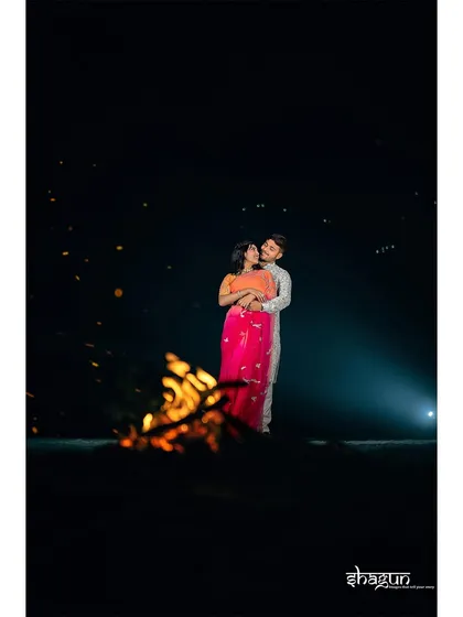 A wide shot of the couple standing by a bonfire, surrounded by darkness. The fire illuminates them, making them the center of their own universe in this dramatic night scene.