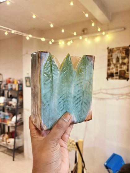 A square vase with a soft green leaf pattern. This piece was hand-built using slabs of clay, showing how you can create geometric forms and add natural textures.