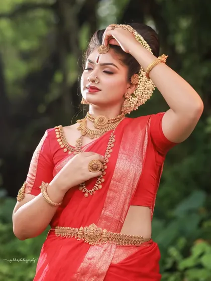 A graceful pose showing the bride adjusting her maang tikka. The sunlight filtering through the trees creates a beautiful, natural light that enhances her features.