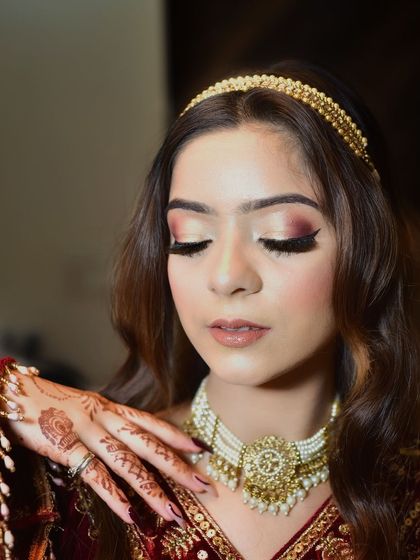 A beautiful close up focusing on the delicate henna design and the traditional pearl necklace. The soft expression and closed eyes create a serene and graceful mood.