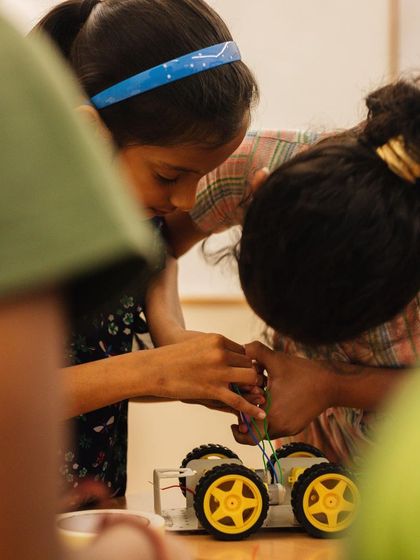 Two students lean in to get a closer look at their robotic car. This collaborative problem-solving is a key part of our learning-by-doing approach.