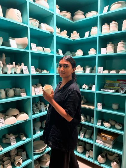 Surrounded by shelves of possibilities, a guest holds up a plain white mug, ready to be transformed into her unique creation.