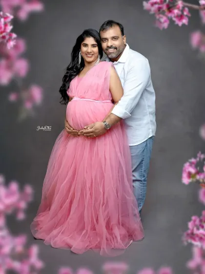 A classic couple's pose against a soft, floral-framed backdrop. The mom to be is glowing in this beautiful pink tulle gown.