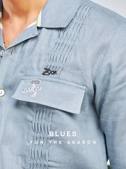My kind of weekend blues. This close-up shows the fine pintuck details and custom ZOOP pin on a light blue shirt, perfect for owning your summer look.