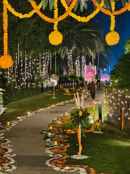 A stunning entrance and walkway for a large-scale outdoor Diwali party. We used extensive flower rangoli, hanging marigold garlands, and warm fairy lights to create a grand and welcoming path for guests.
