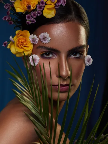 A creative floral look with yellow and purple flowers arranged in the hair, paired with a subtle yet defined eye makeup.