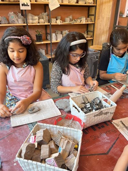 Our summer camp tables are always a hub of activity. Here, a group of girls are using stamps and tools to add texture to their clay slabs, learning new hand-building techniques together.