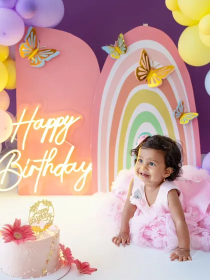 A beautiful shot of the birthday girl in a fluffy pink dress, crawling towards her cake against the pastel rainbow backdrop.