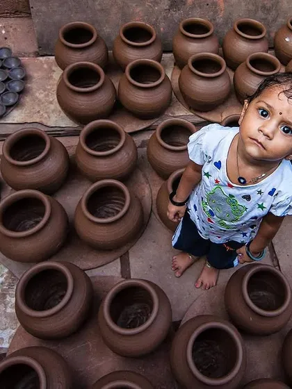 A small child looks up from a sea of freshly made clay pots, her curious gaze creating a powerful connection. This overhead shot contrasts the innocence of youth with the world of labor she is growing up in.