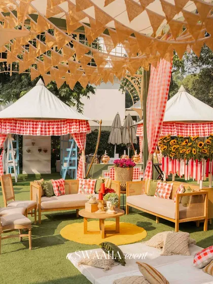 The lounge area for the baby shower, with rustic wooden furniture, checkered cushions, and a canopy of bunting flags, creating a relaxed and playful vibe.