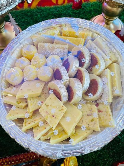 A delicious assortment of traditional Indian sweets, beautifully arranged on a silver plate. I can provide a wide variety of sweets to make your celebration even more special.
