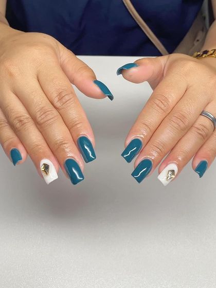 A chic set with teal nails and white accent nails featuring gold charms. This is a great example of using hardware to elevate a design.