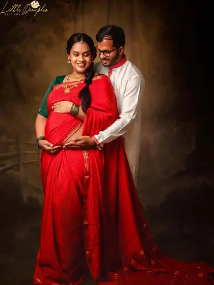 Another beautiful pose from this traditional maternity shoot, showcasing the flowing fabric of the saree and the couple's gentle interaction.