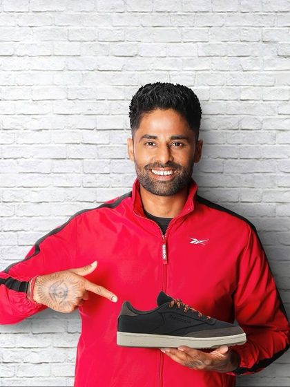 A clean, direct-to-camera shot for a Reebok campaign with Suryakumar Yadav. He's styled in a simple red and black jacket, pointing to the shoe, making the product the hero of the image.